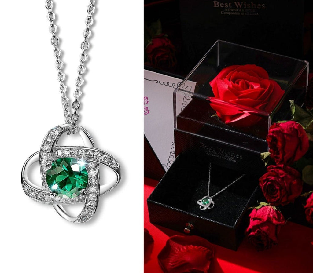 Silver necklace with a green gemstone in front of a box with red roses.