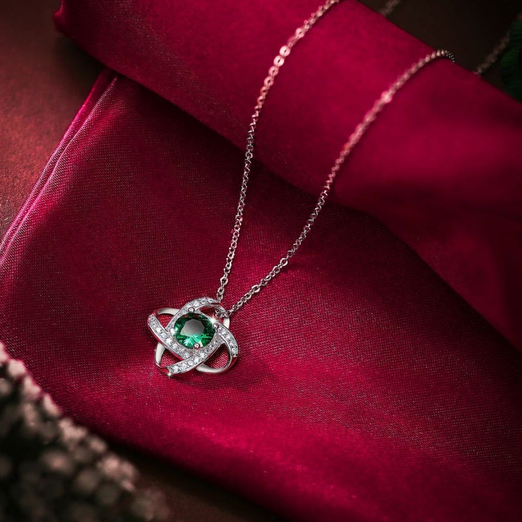 Silver necklace with a green gemstone pendant on a red fabric background