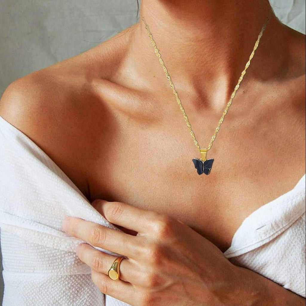 Gold necklace with a butterfly pendant worn by a person, with a neutral background.